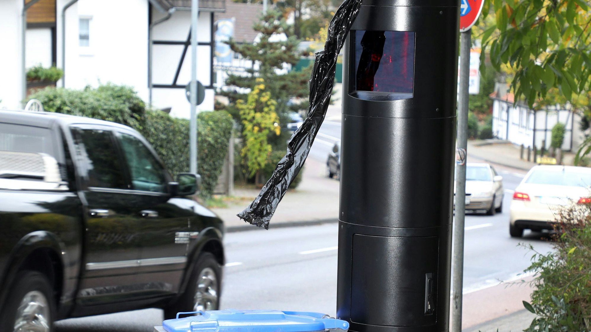 Eine moderne Radarsäule steht an einer Straße. Auf der Fahrbahn fährt ein schwarzes Auto.