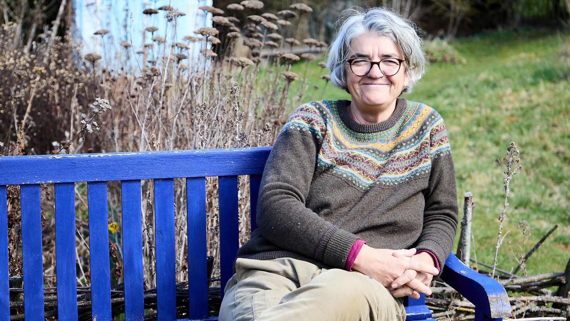 Ulrike Kreuer sitzt in ihrem Garten in Nettersheim auf einer blauen Bank.