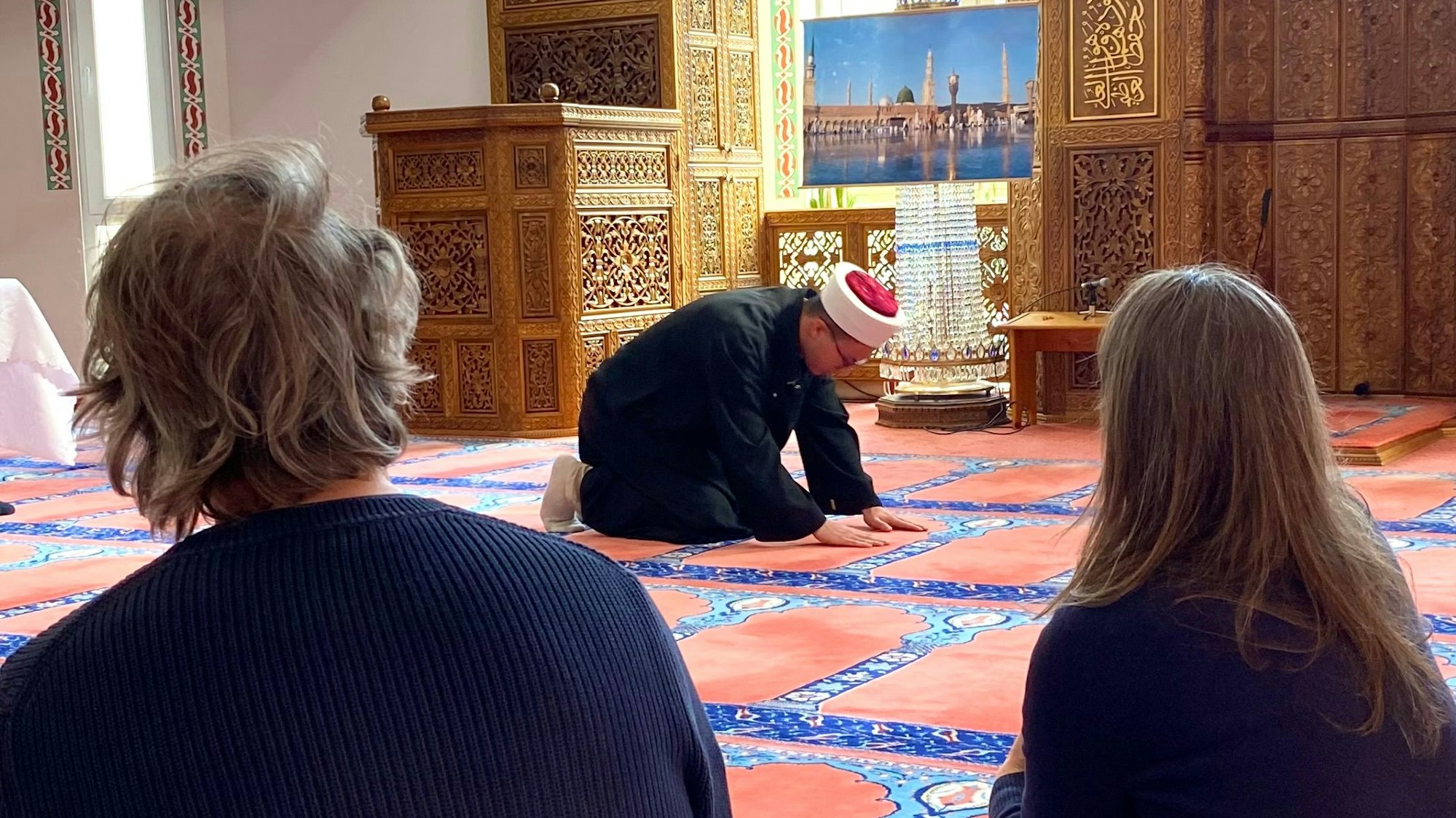 Ein Mann kniet zum Gebet auf einem Teppich in einer Moschee.