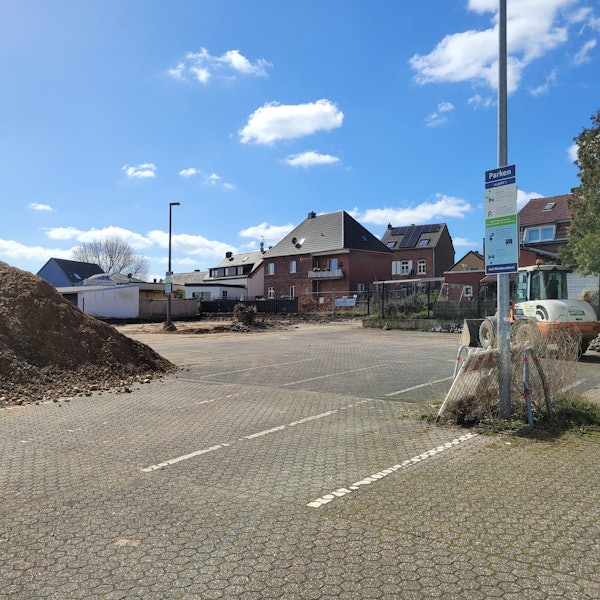 Ein Parkplatz, links ein Erdhaufen, im Hintergrund rechst ein Bagger.