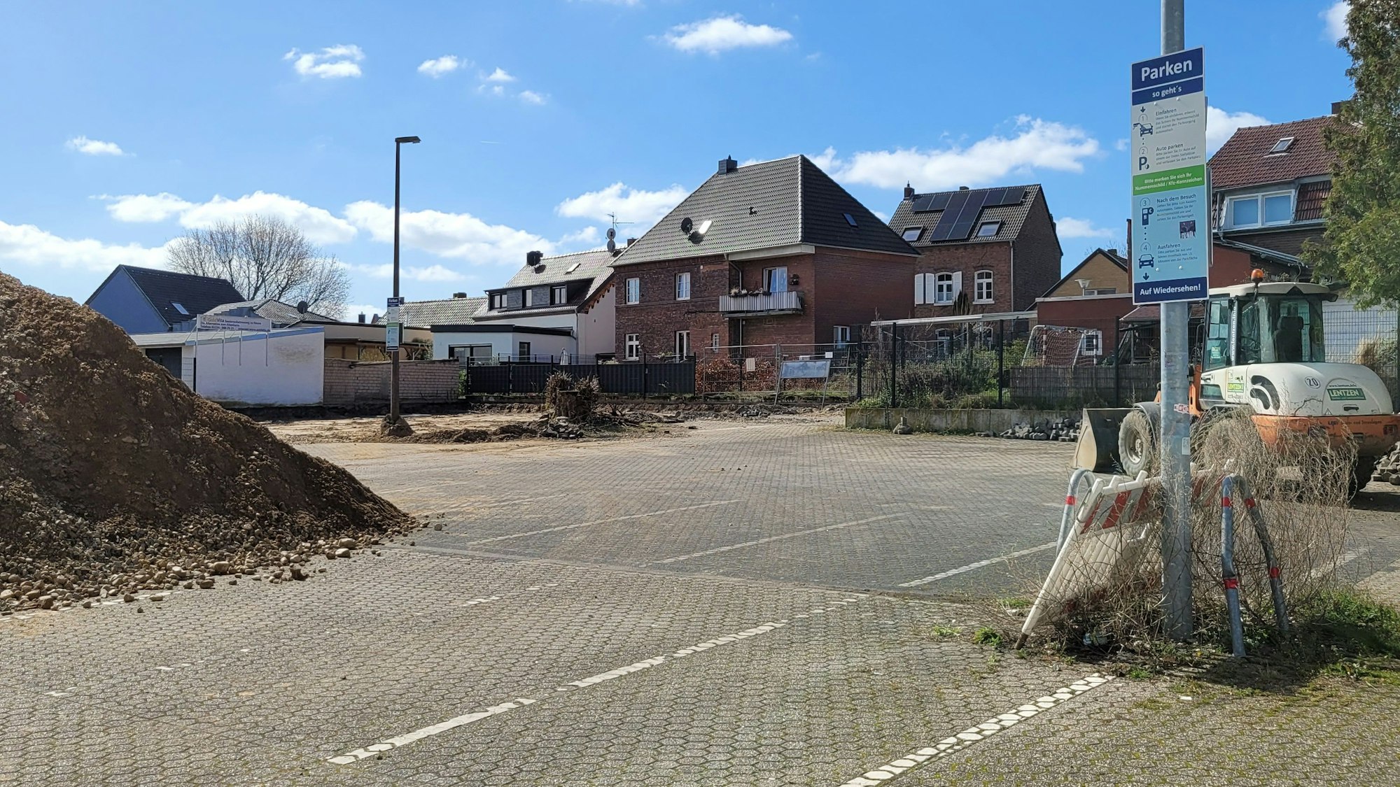 Ein Parkplatz, links ein Erdhaufen, im Hintergrund rechst ein Bagger.