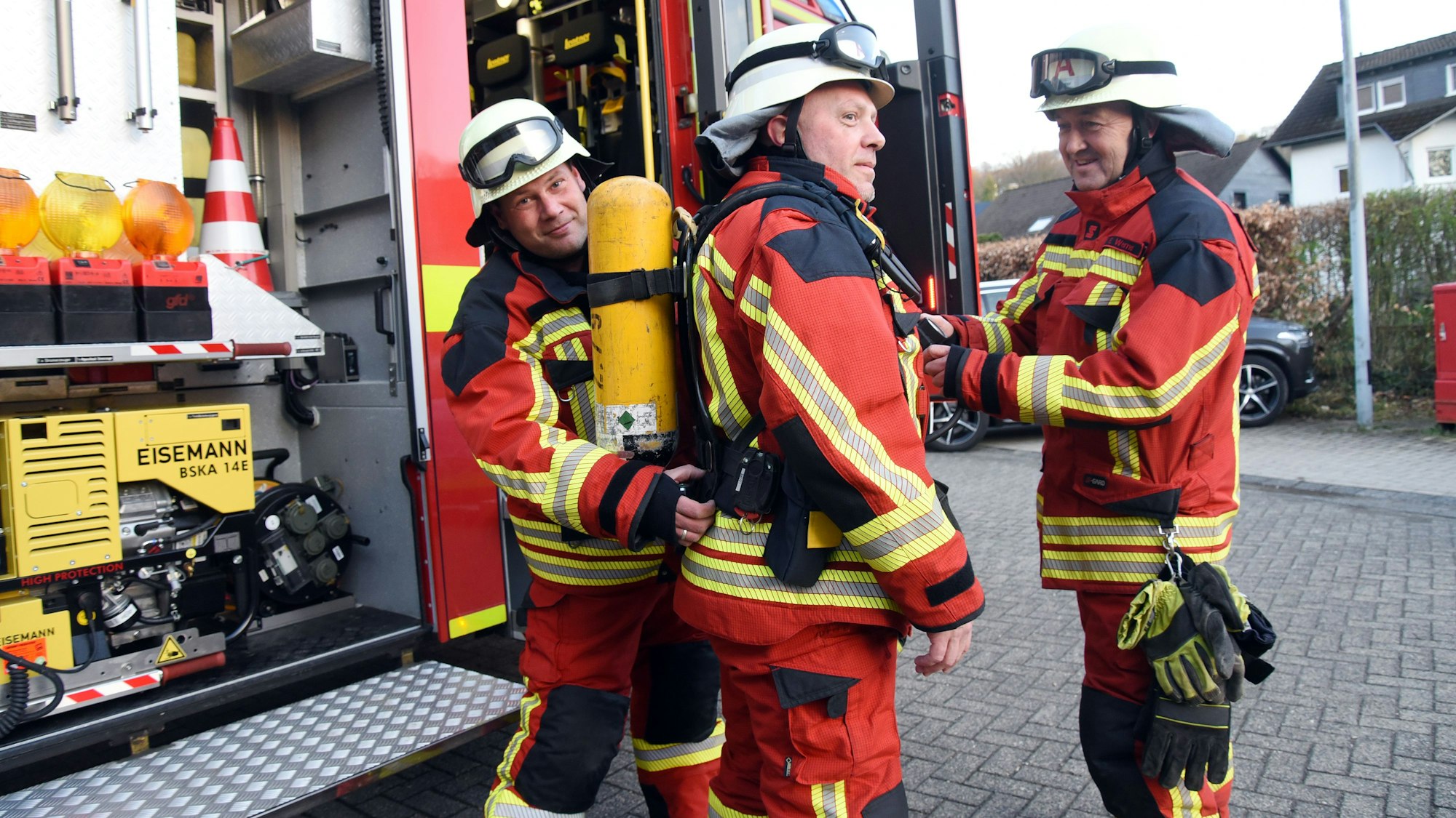 Drei Feuerwehrleute stehen an einem Feuerwehrauto.