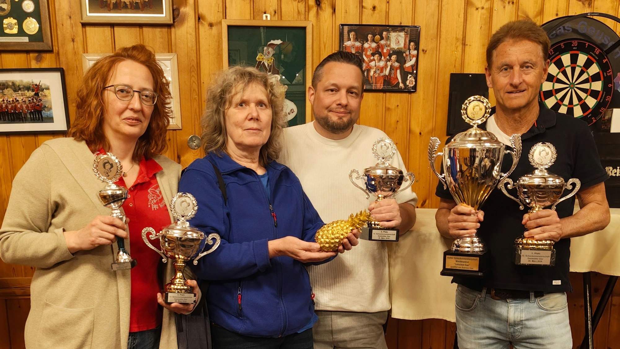 Das Bild zeigt zwei Frauen und zwei Männer. Sie halten Pokale in den Händen, eine Frau hält eine goldene Ananas.