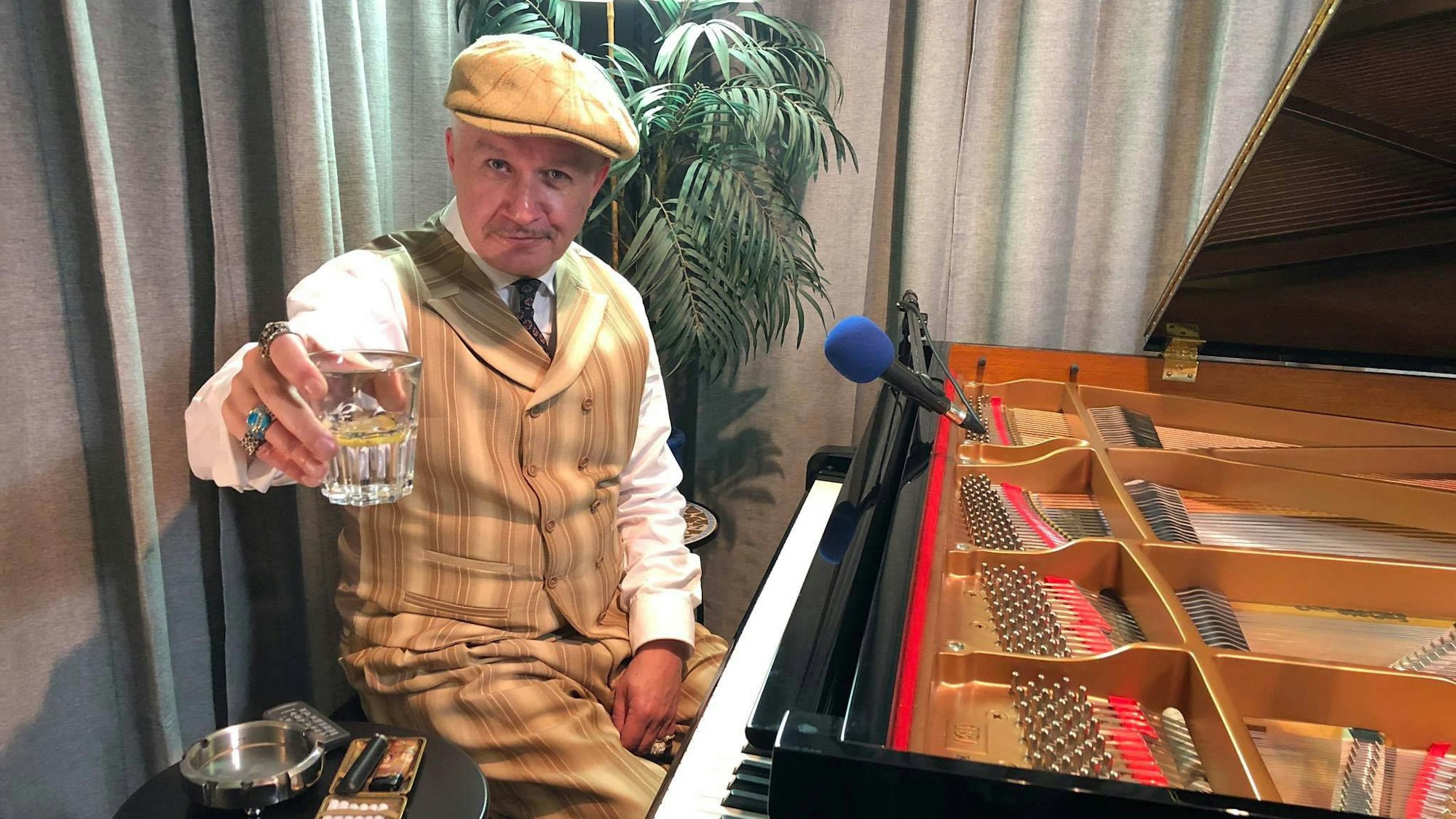 Christian Christl sitzt am Piano und hält ein Glas in die Kamera.