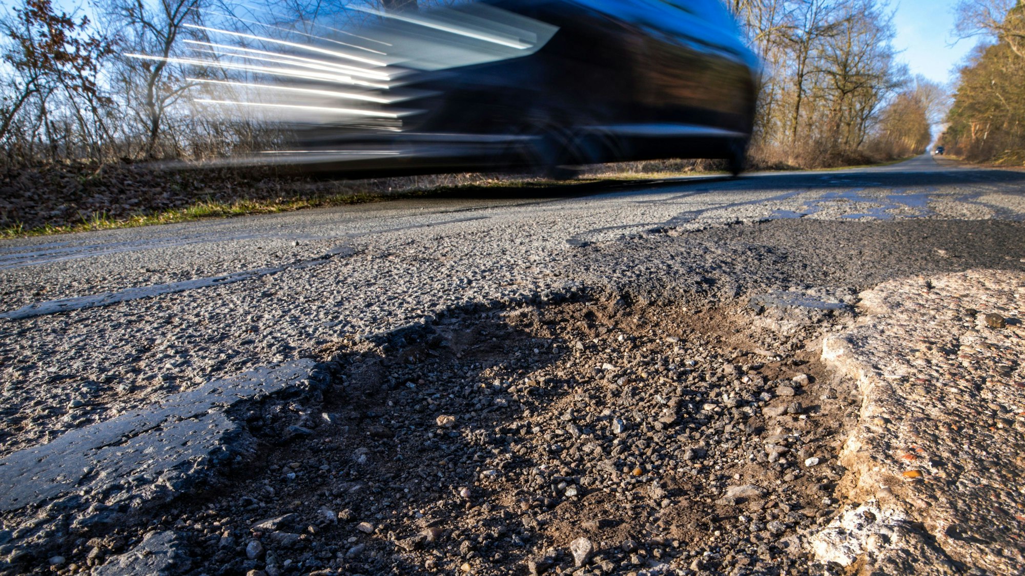 Das Foto zeigt ein Auto, das an einem Schlagloch vorbeifährt.