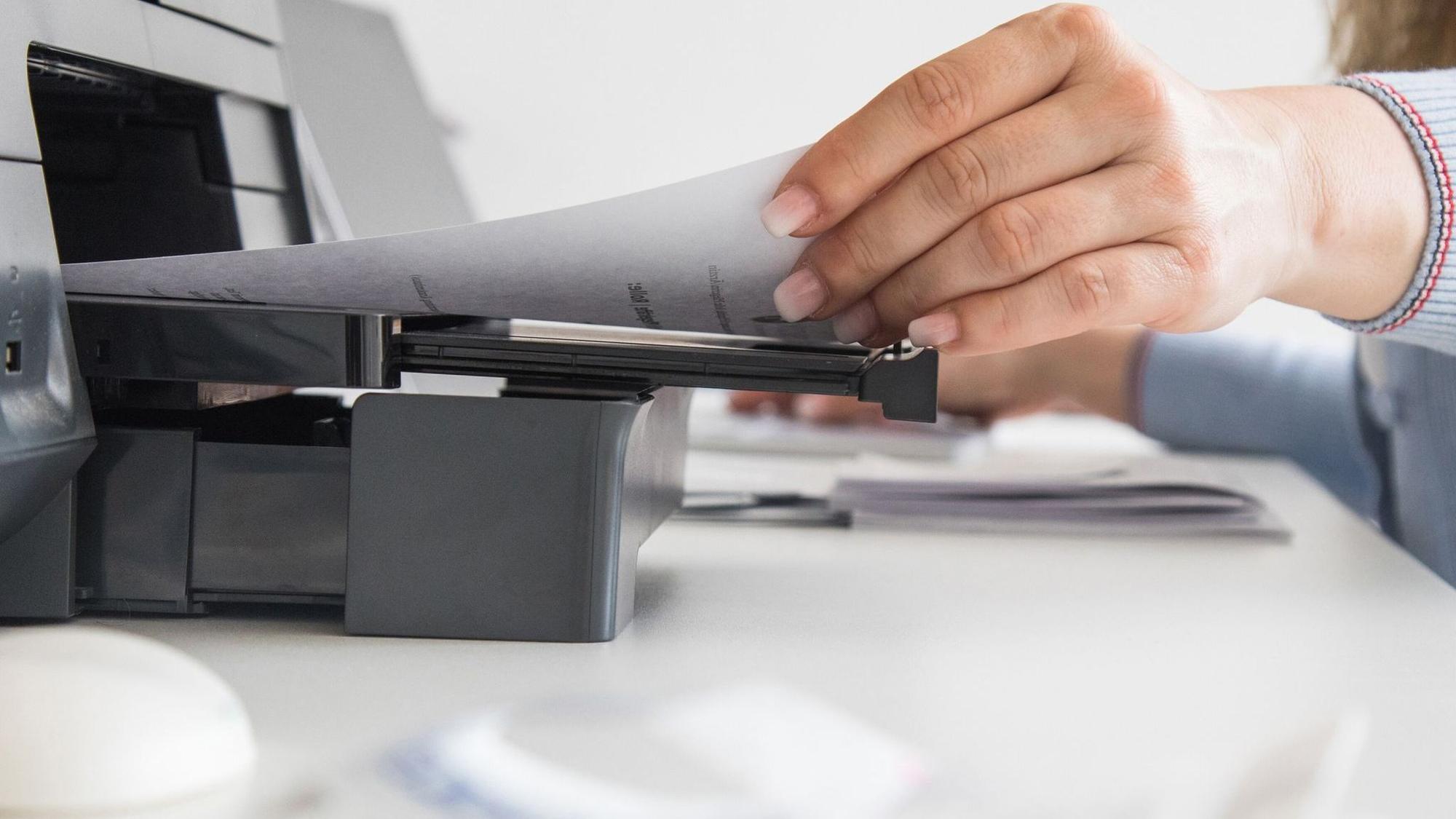 Frau nimmt ein Blatt Papier aus einem Drucker