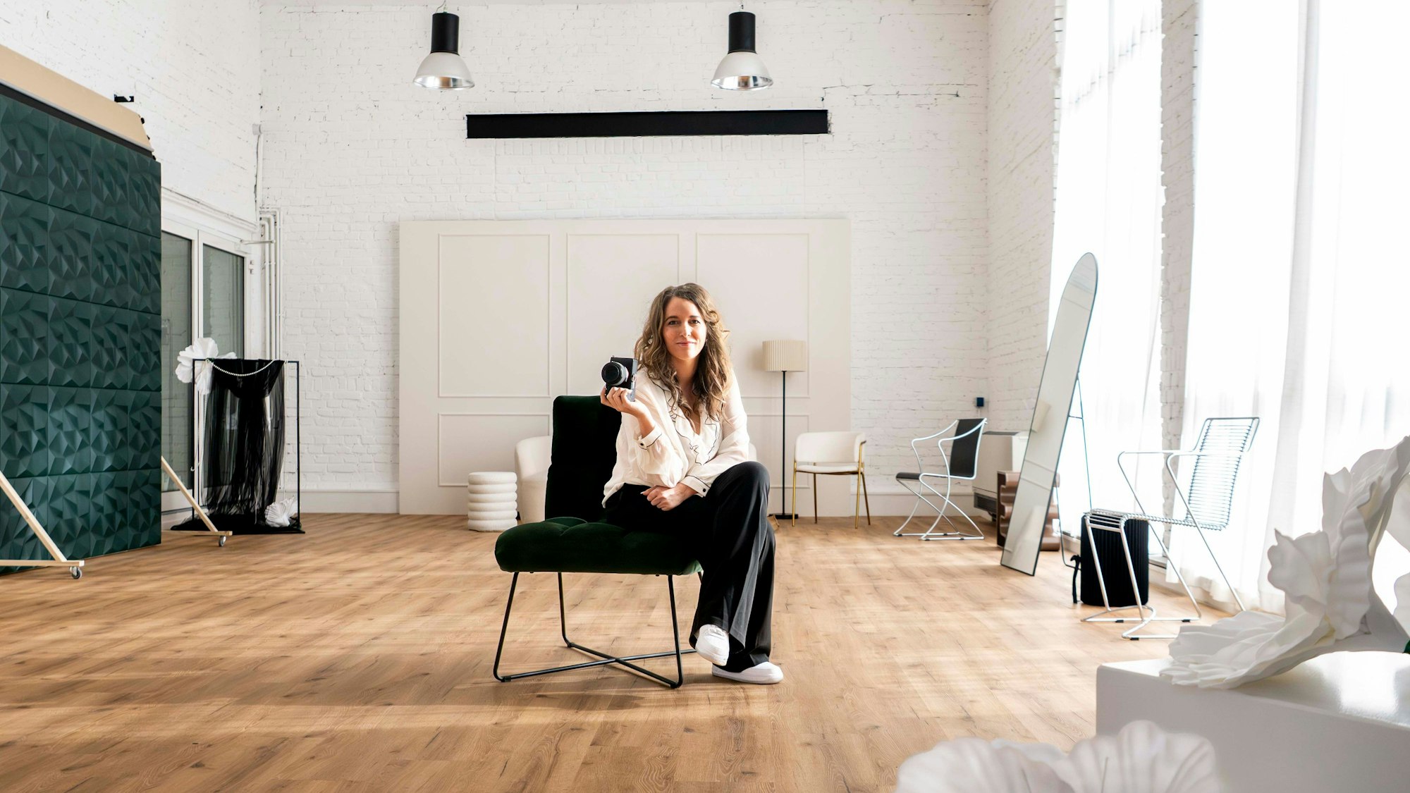 Sarah Pfeiffer-Schröder sitzt in ihrem Studio auf einem Stuhl, in der Hand hält sie eine Kamera.