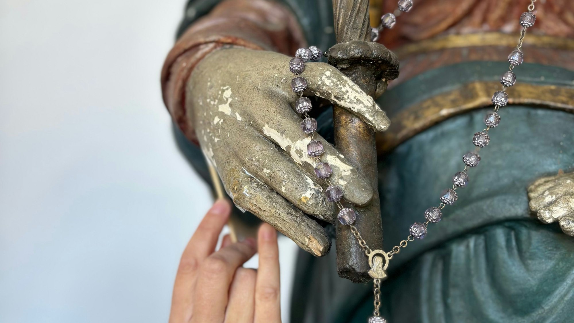 Nahaufnahme auf eine Hand die einen Wattestab an die Hand einer Marien-Figur anlegt.