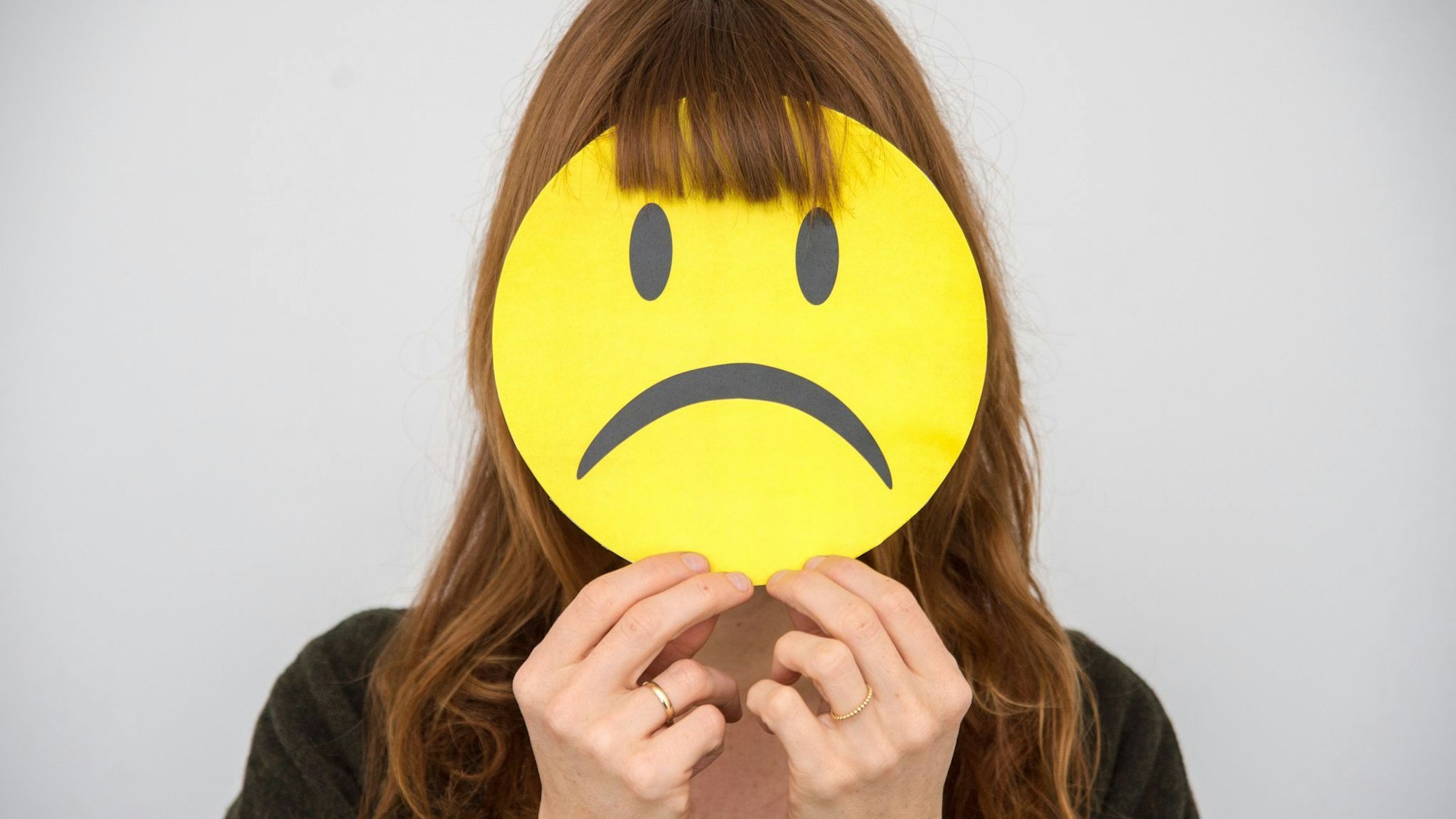 Eine Frau hält sich ein trauriges Smiley vor ihr Gesicht