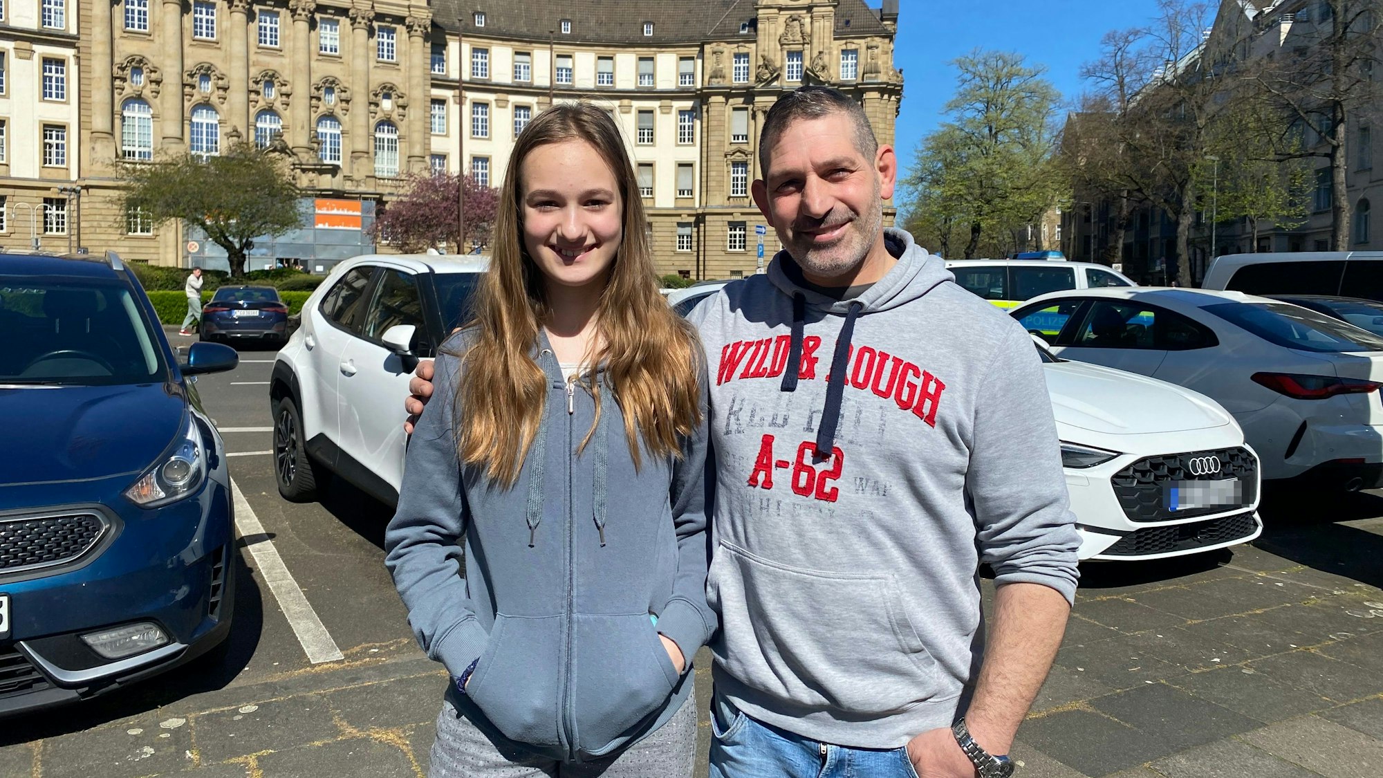 Ein Mädchen und ein Mann lächeln Arm in Arm in die Kamera.