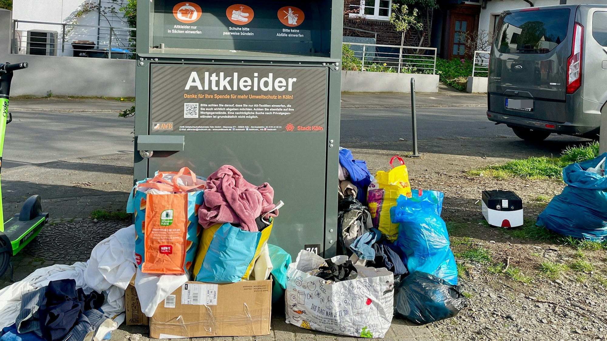 Ein AWB-Altkleidercontainer am Sürther Marktplatz, davor Tüten voller Kleidung.
