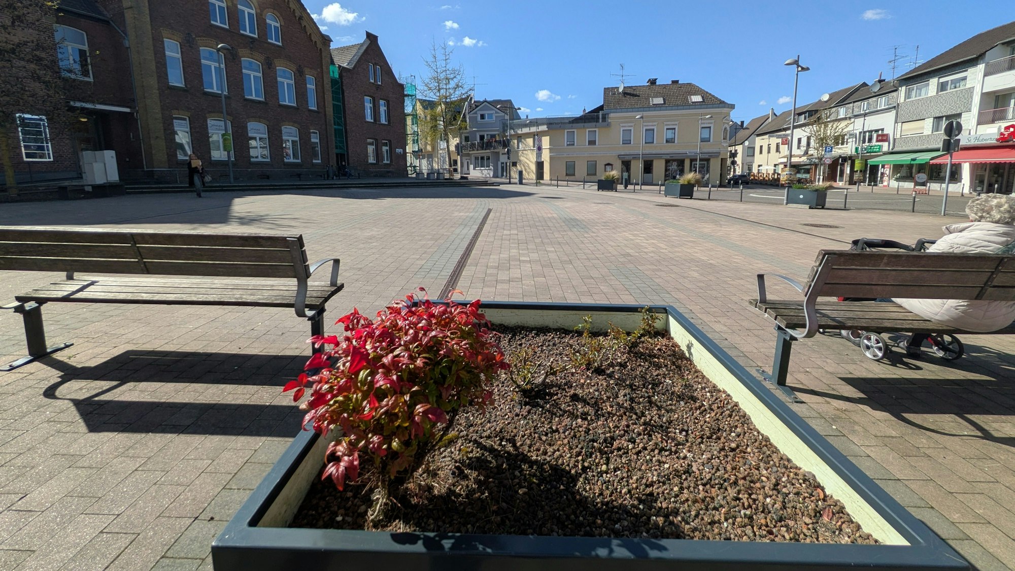 Blick auf den Peter-Fryns-Platz in Bornheim: Im Vordergrund liegt ein ummauertes Blumenbeet inmitten von zwei Sitzbänken.