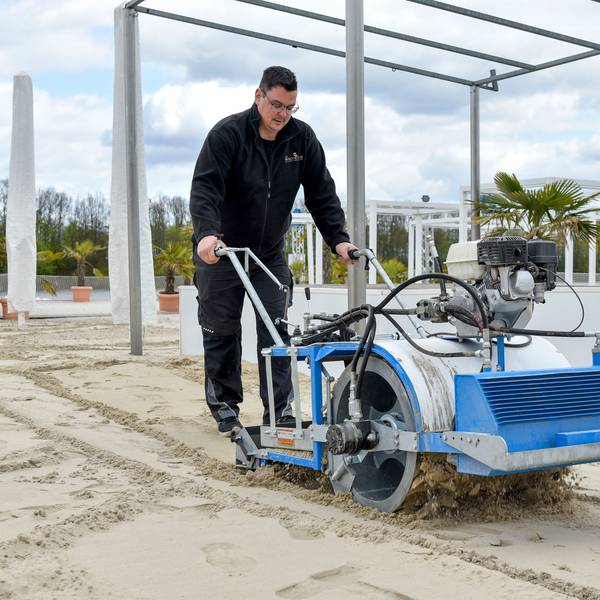 Zu sehen ist ein Mann, der eine Sandreinigungsmaschine schiebt.