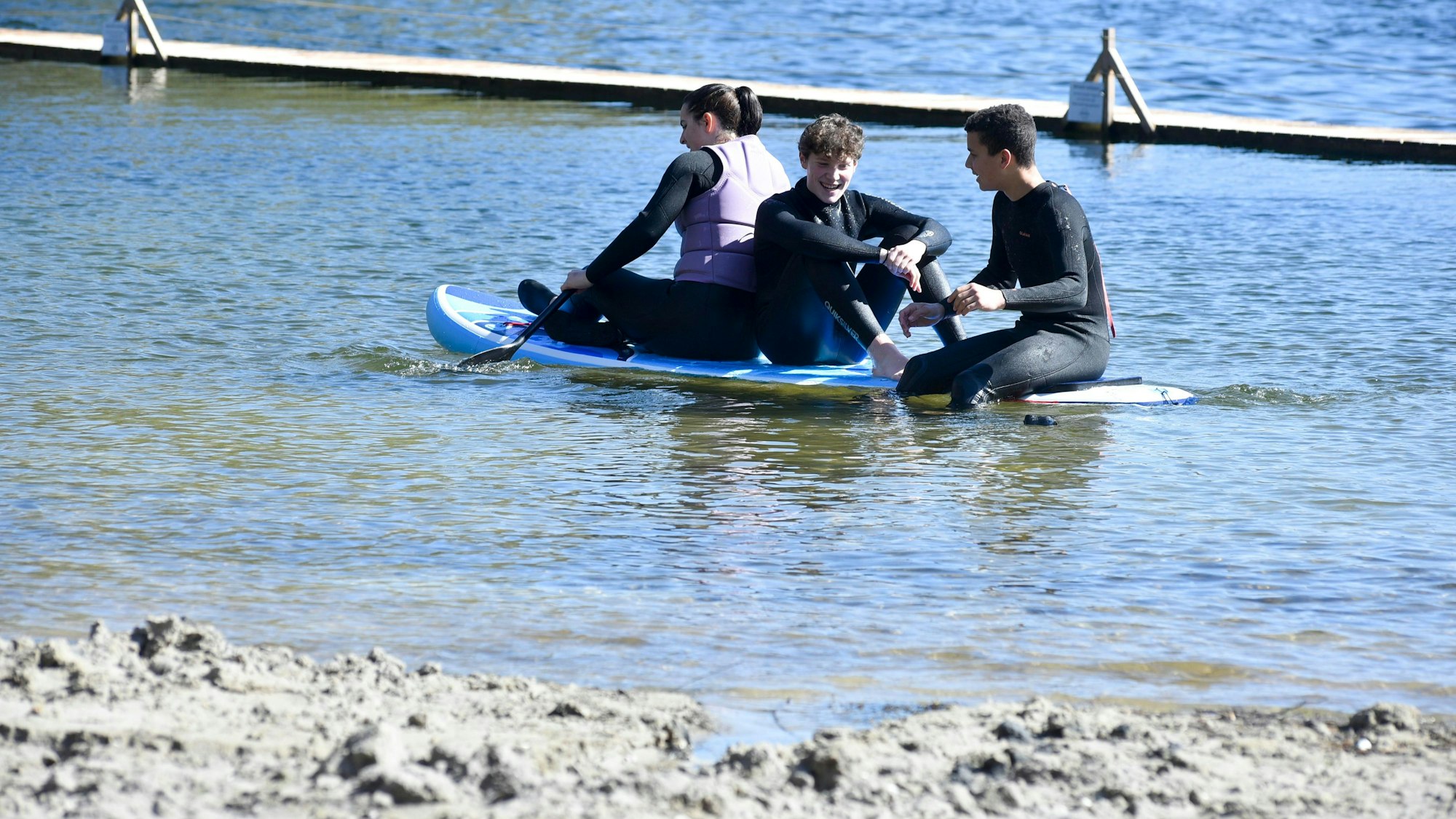 Zu sehen sind drei junge Männer auf einem Surfboard.