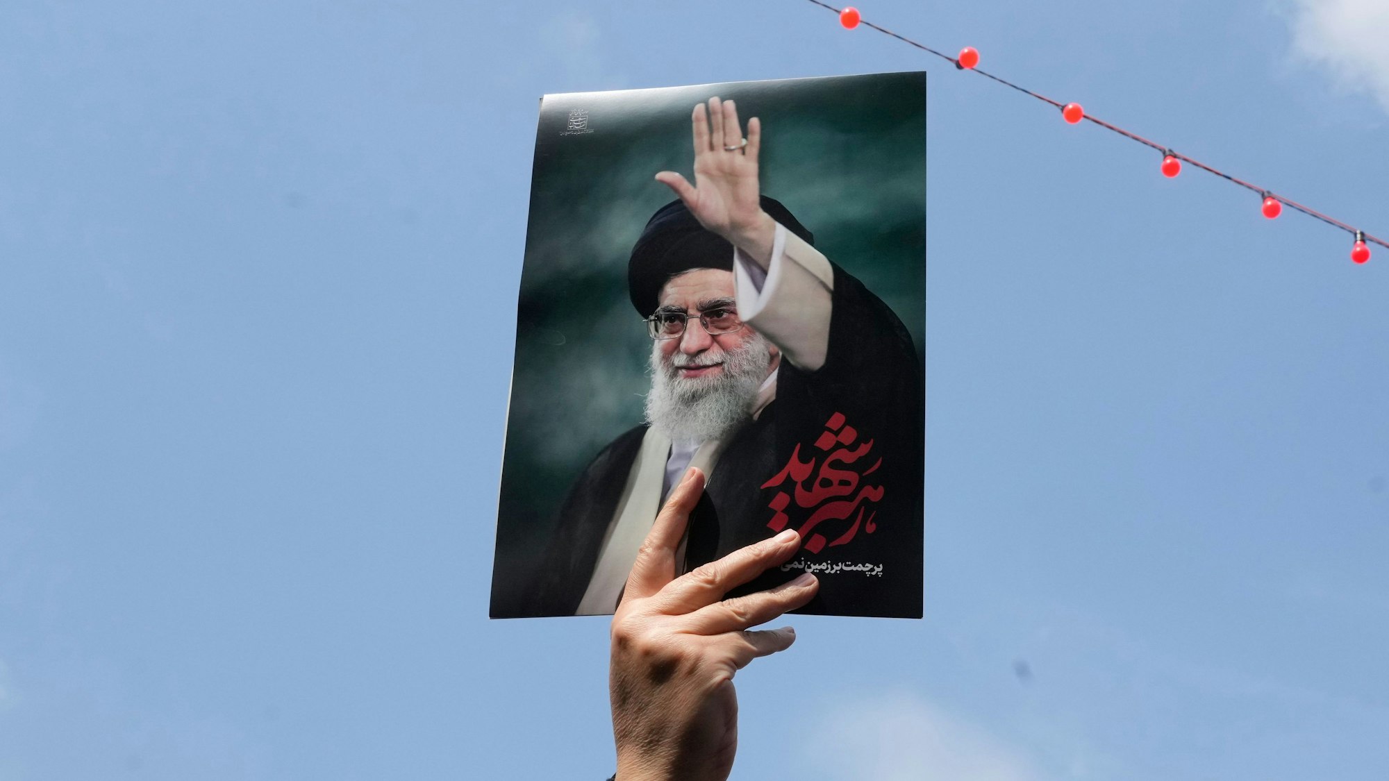 Eine Frau hält ein Poster des verstorbenen iranischen Obersten Führers Ajatollah Ali Chamenei in die Höhe, während sie am Trauerzug für hochrangige iranische Militärs und Zivilisten teilnimmt.