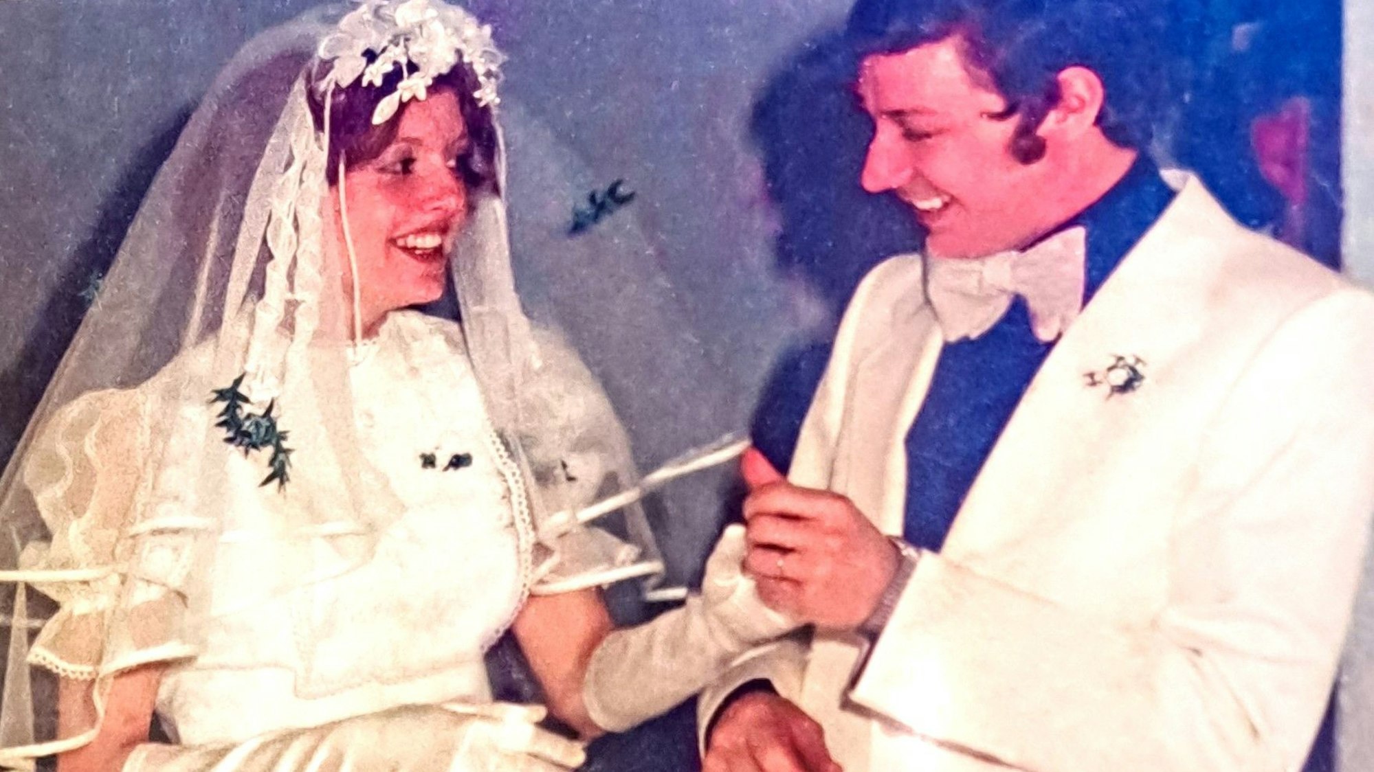 Das Bild zeigt ein Ehepaar in Weiß an seinem Hochzeitstag.