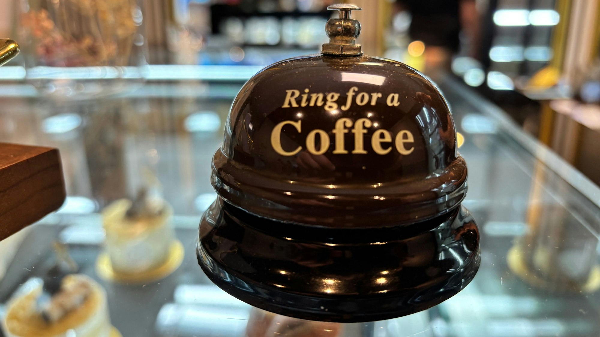Auf einem gläsernen Thresen steht eine Klingel mit der Aufschrift: „Ring for a Coffee“.