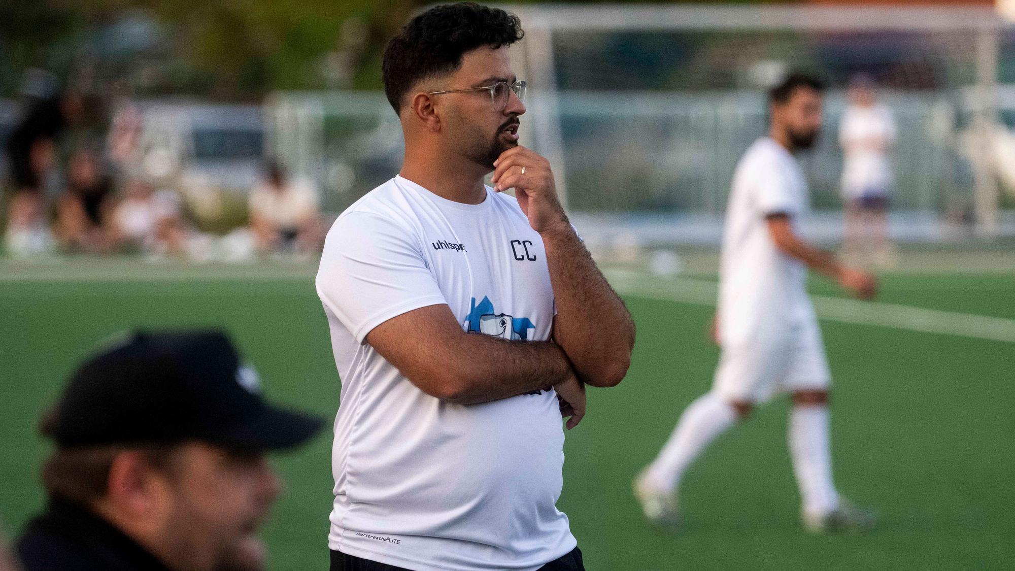Bessenichs Trainer Can Celik beobachtet ein Spiel seiner Mannschaft, hat eine Hand vor der Brust und eine am Kinn.