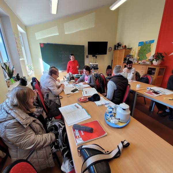 Frauen und Männer im Deutschunterricht, im Hintergrund die Lehrerin Iris Braun.