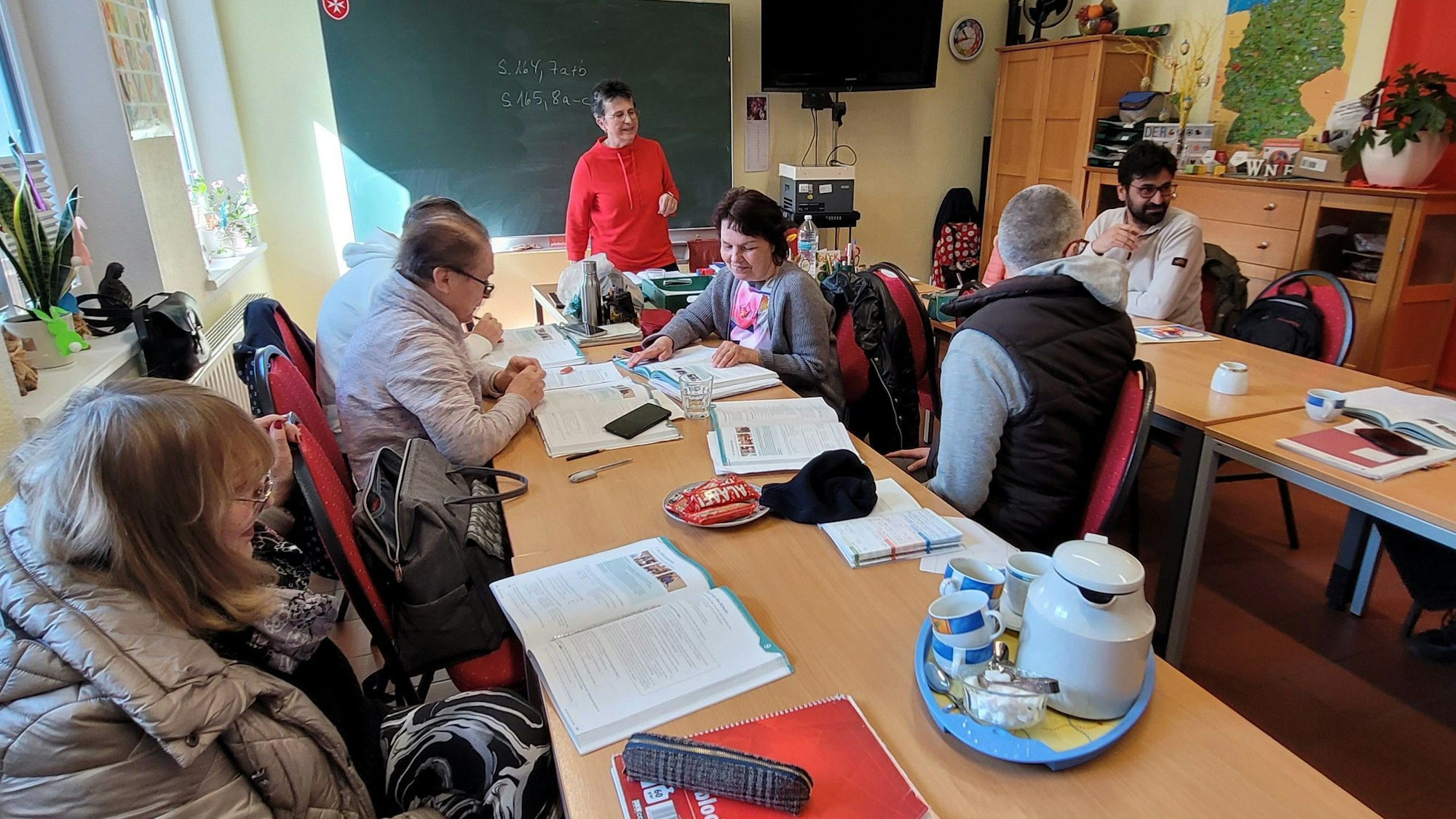 Frauen und Männer im Deutschunterricht, im Hintergrund die Lehrerin Iris Braun.