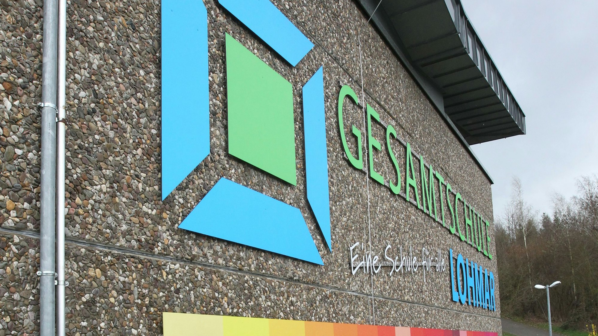 Der Schriftzug der Gesamtschule Lohmar steht neben einem dazugehörigen Logo auf der Wand das Schulgebäudes.
