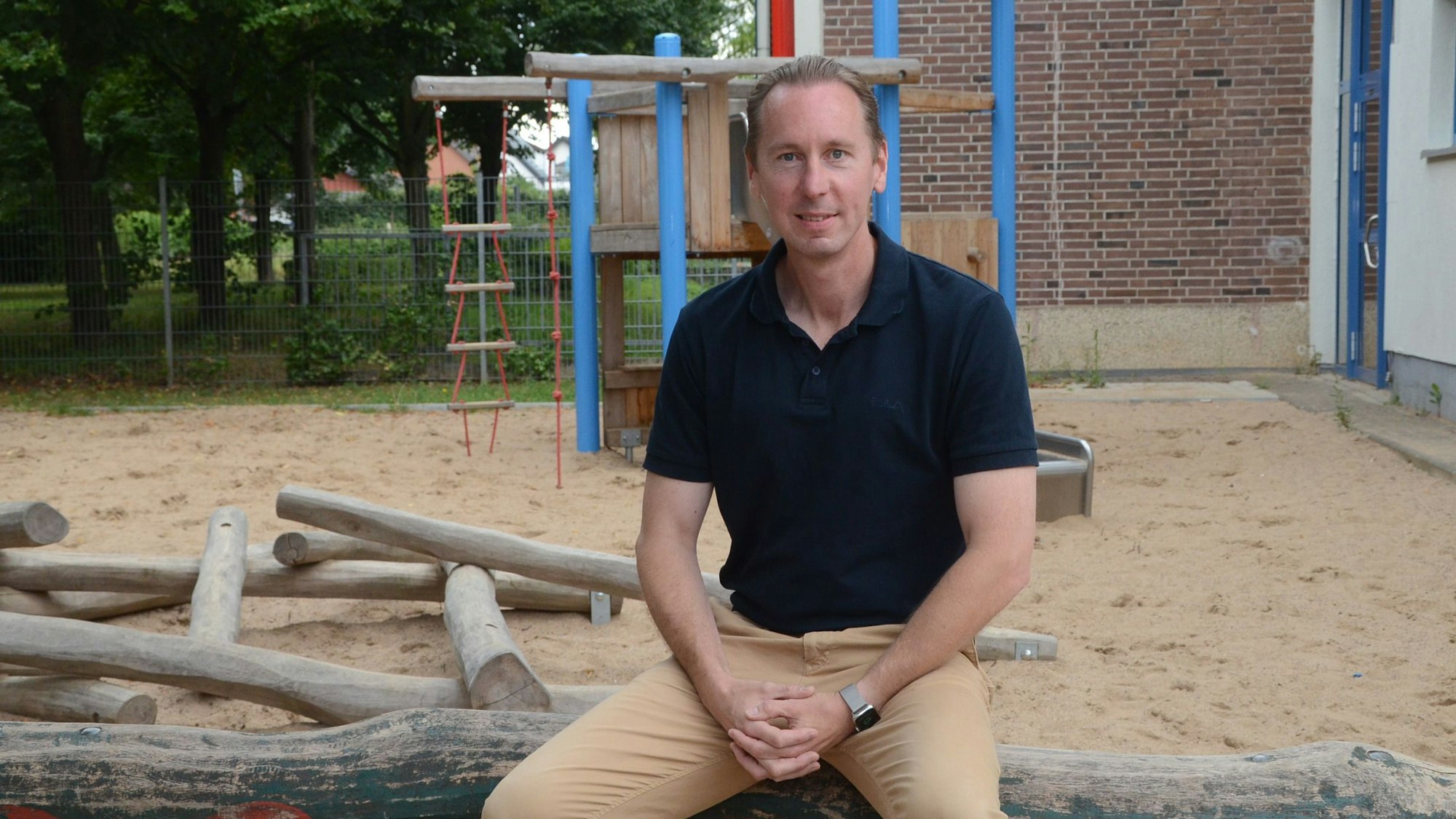 René Wirtz, Fraktionsvorsitzender der SPD in Troisdorf, sitzt auf einem Baumstamm an einem Spielplatz.
