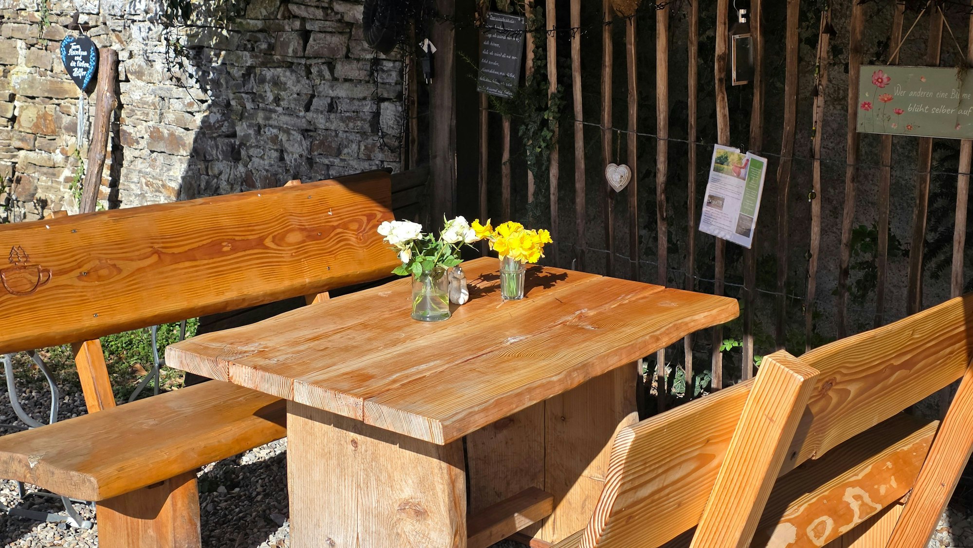 Ein Tisch mit Blumen und Bänken steht in der Sonne.