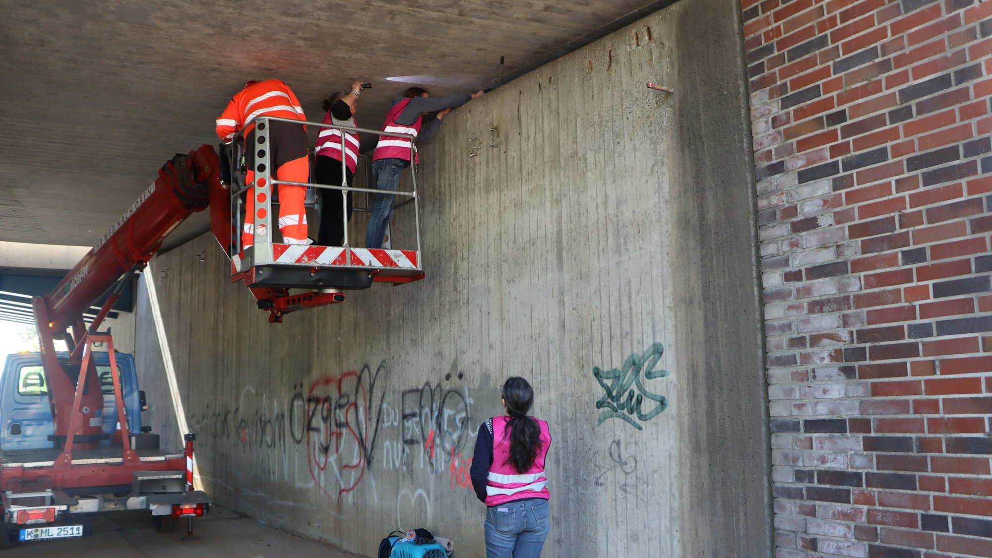 Menschen stehen im Tragekorb eines Hubwagens unter einem Brückenwerk.