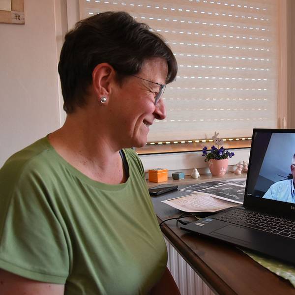 Eine Frau blickt einen Mann auf dem Bildschirm ihres Laptops an, beide lächeln.