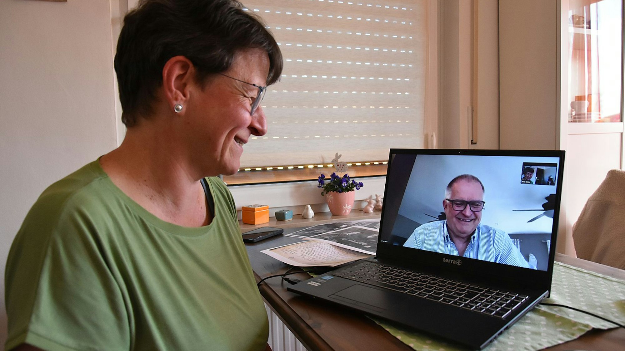 Eine Frau blickt einen Mann auf dem Bildschirm ihres Laptops an, beide lächeln.