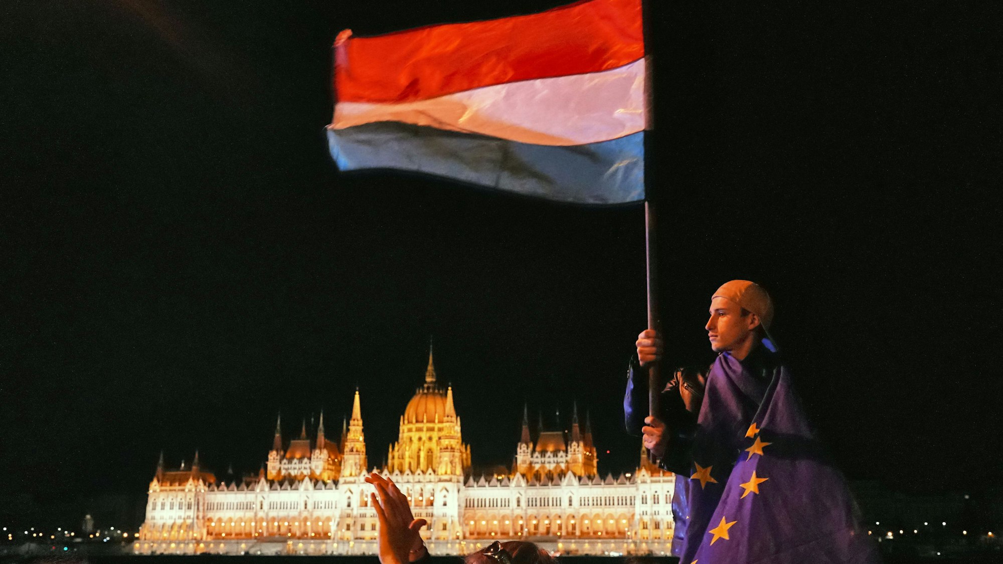 Budapest: Ein in die Flagge der Europäischen Union gehüllter Mann schwenkt am frühen Montag vor dem Hintergrund des Parlamentsgebäudes eine ungarische Fahne.