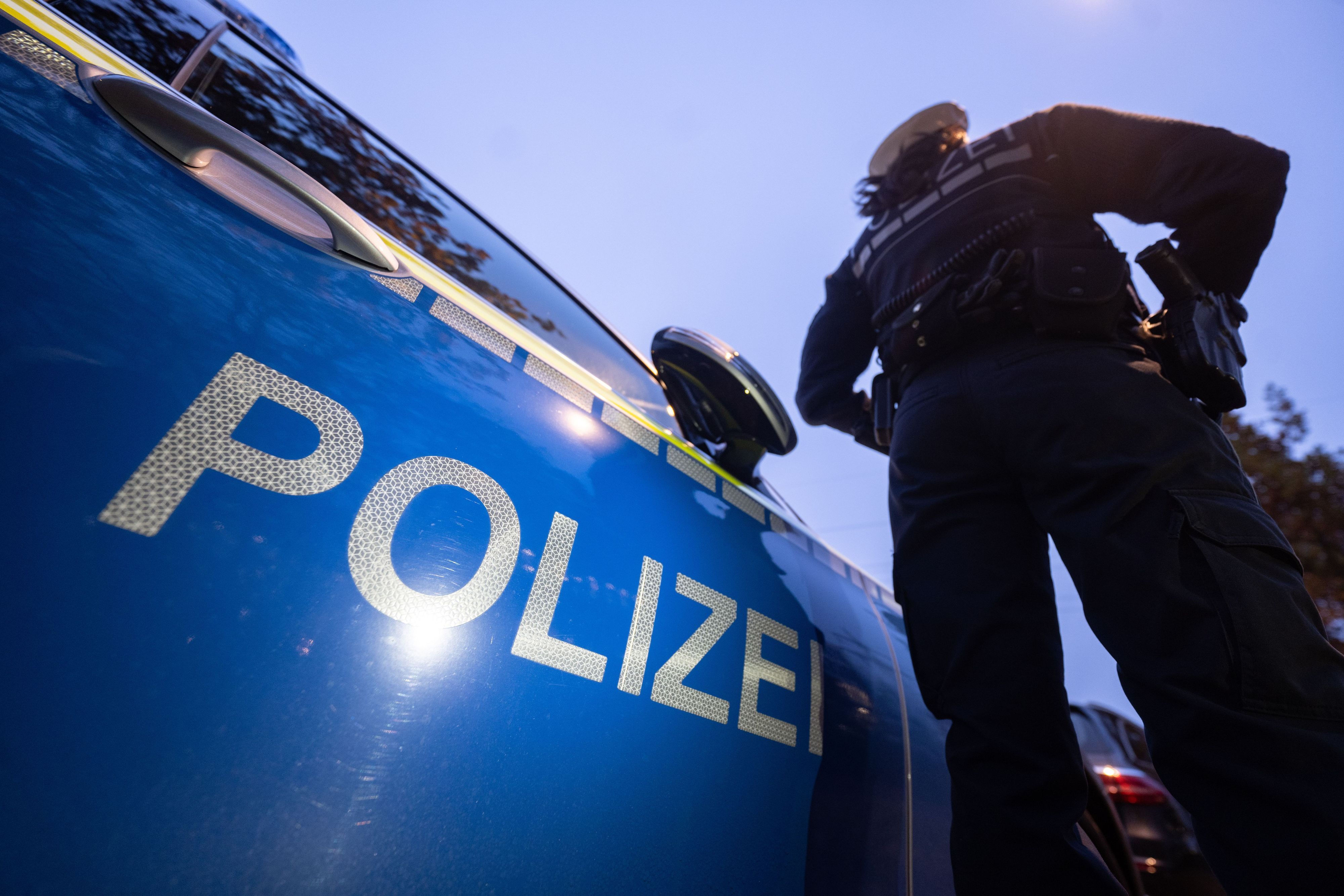 Eine Polizistin steht neben einem Polizeifahrzeug. Mittlerweile wurden drei Tatverdächtige wegen des Mordes an einem 93-jährigen Kölner festgenommen.