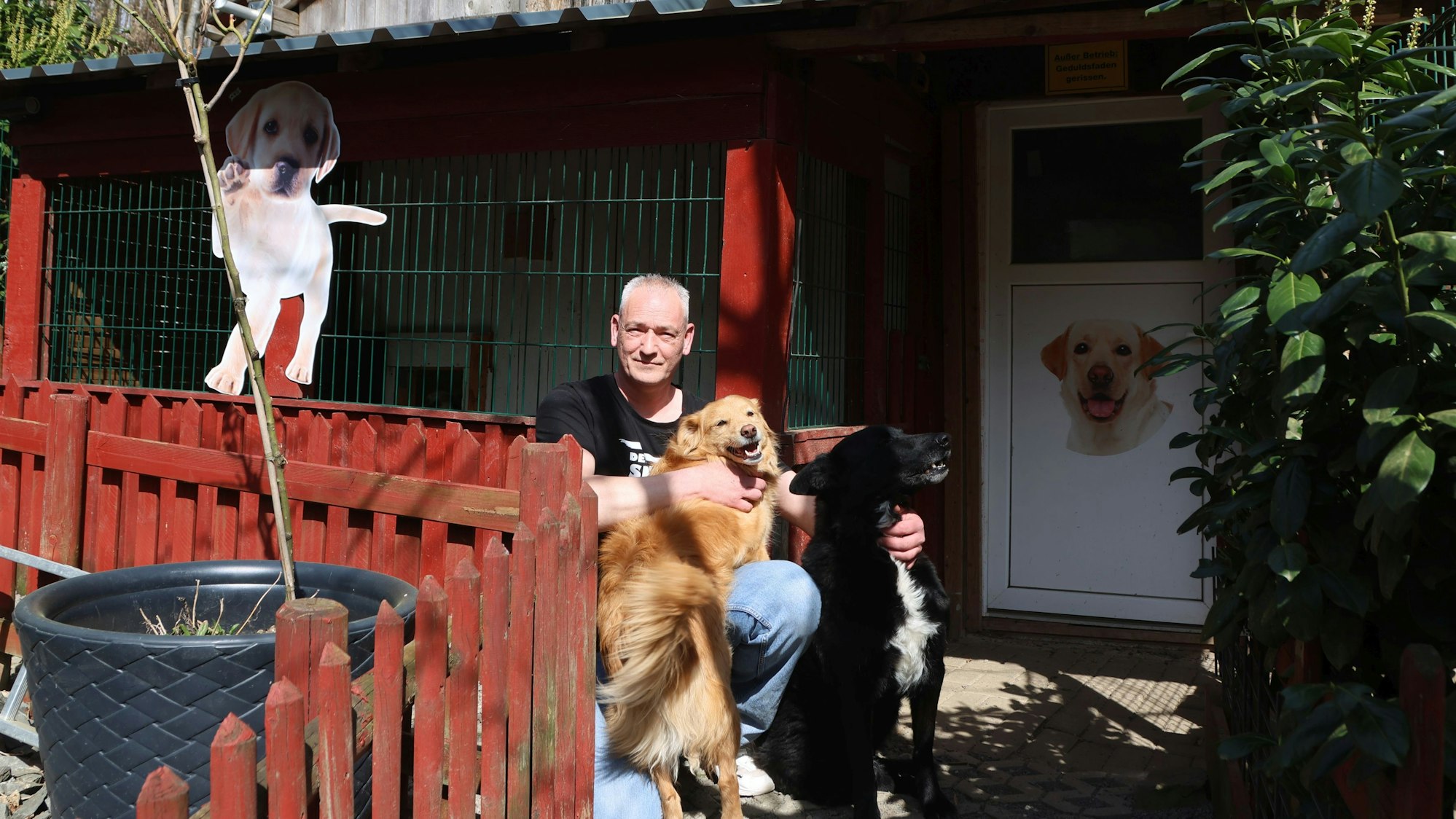 Ein Mann sitzt mit zwei Hunden vor einer Auffangstation für Hunde.