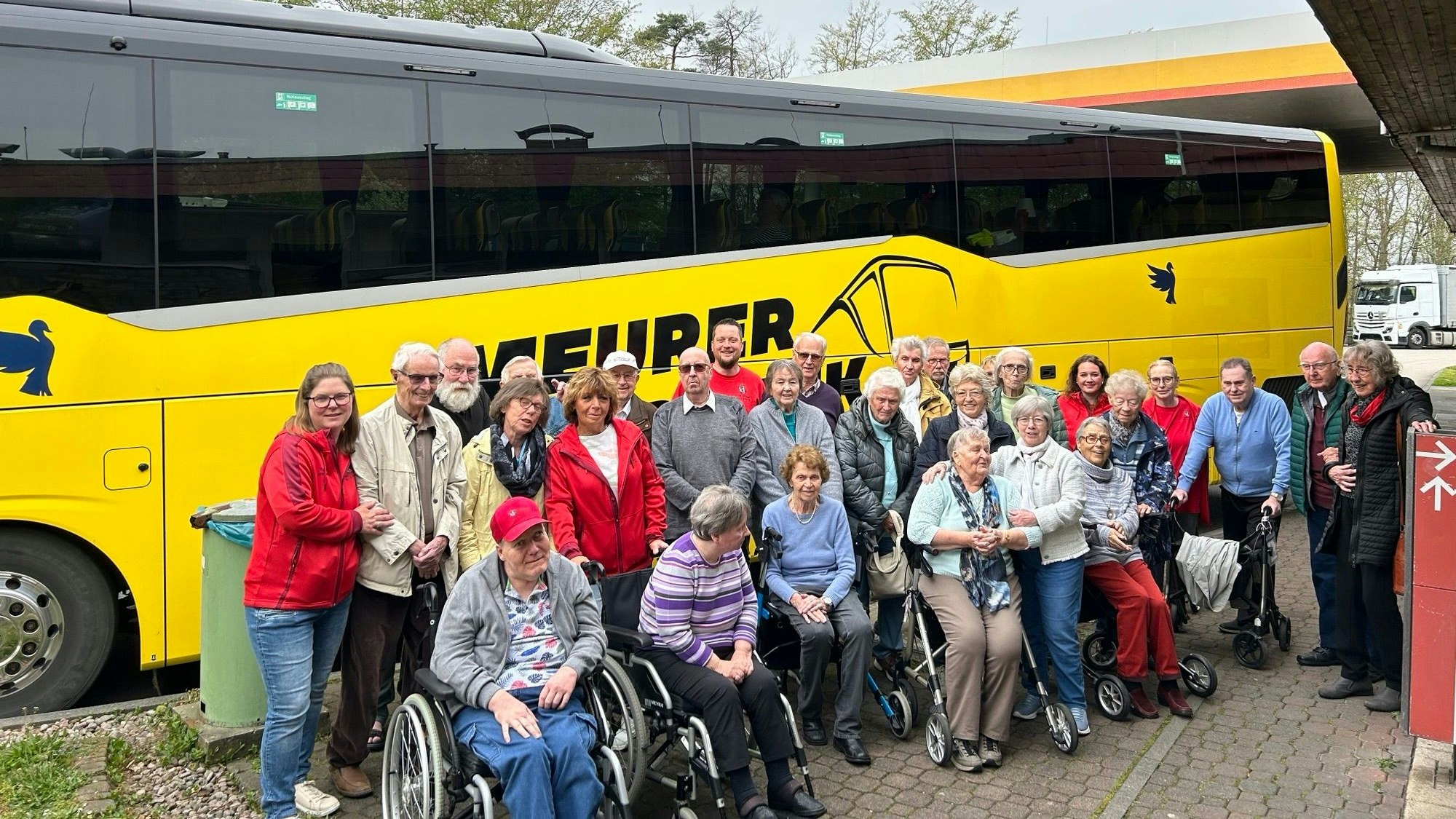 Zu sehen ist eine Gruppe Senioren vor einem Reisebus mit Pflegepersonal.