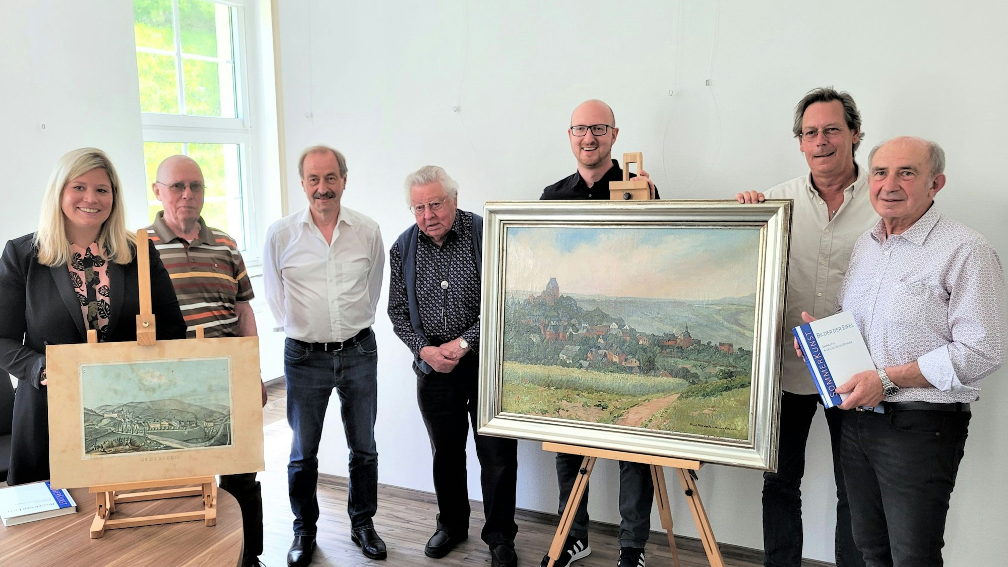 Sieben Männer und eine Frau stehen nebeneinander und präsentieren ein Ölgemälde und eine Zeichnung.