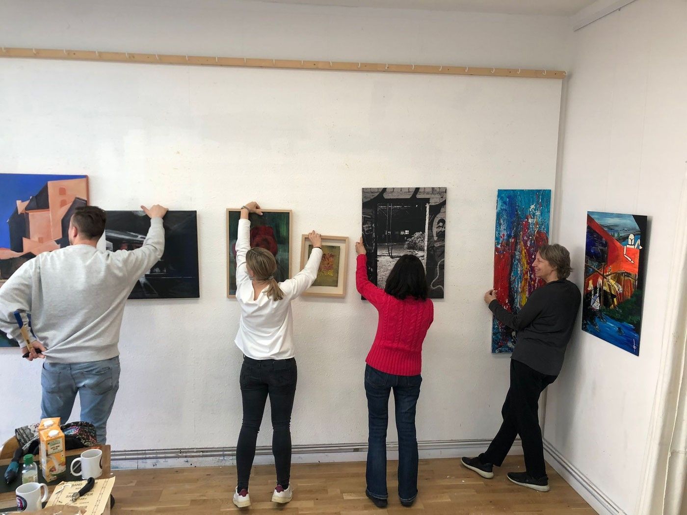Einige Künstlerinnen und Künstler hängen gemeinsam im Atelier Köln Süd ihre Bilder für eine Ausstellung auf.