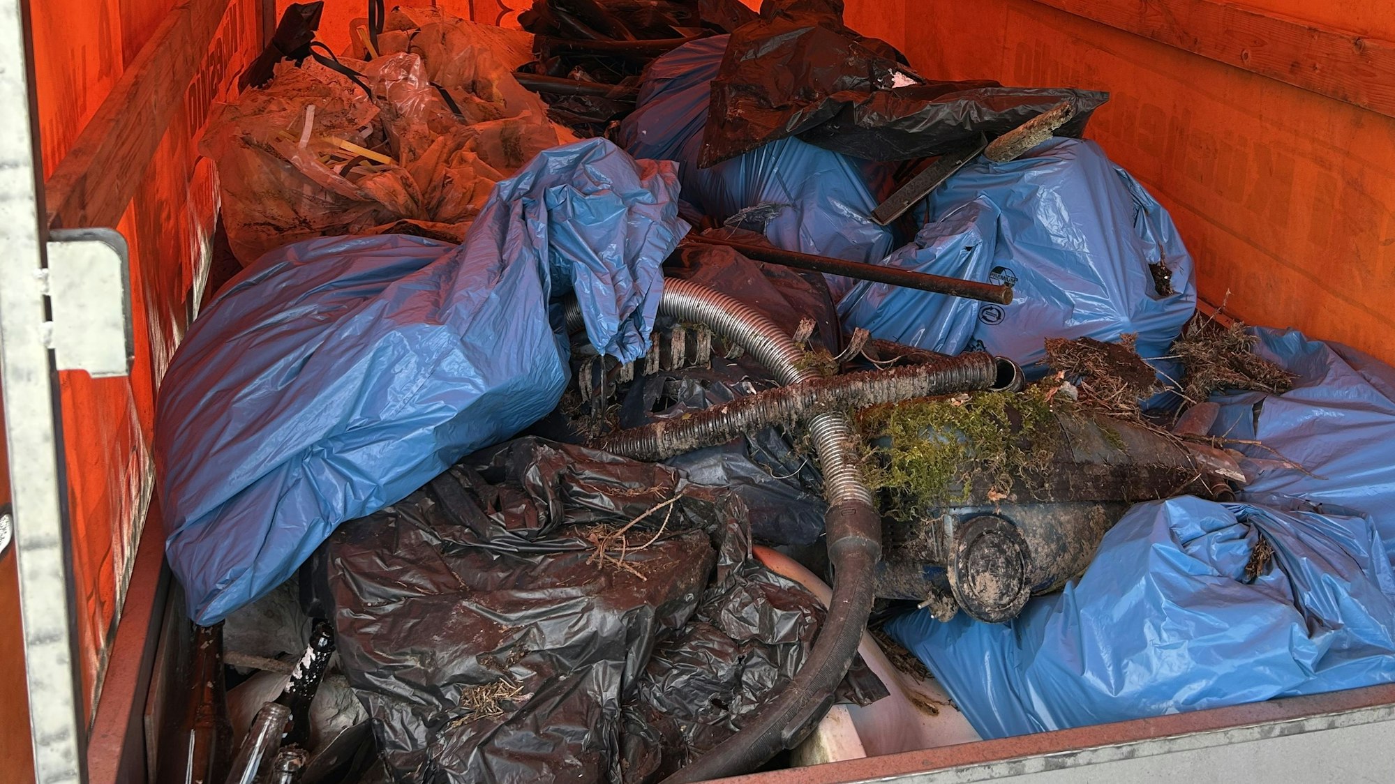 Mehrere blaue Müllsäcke und sonstiger Unrat liegen auf einem Hänger.