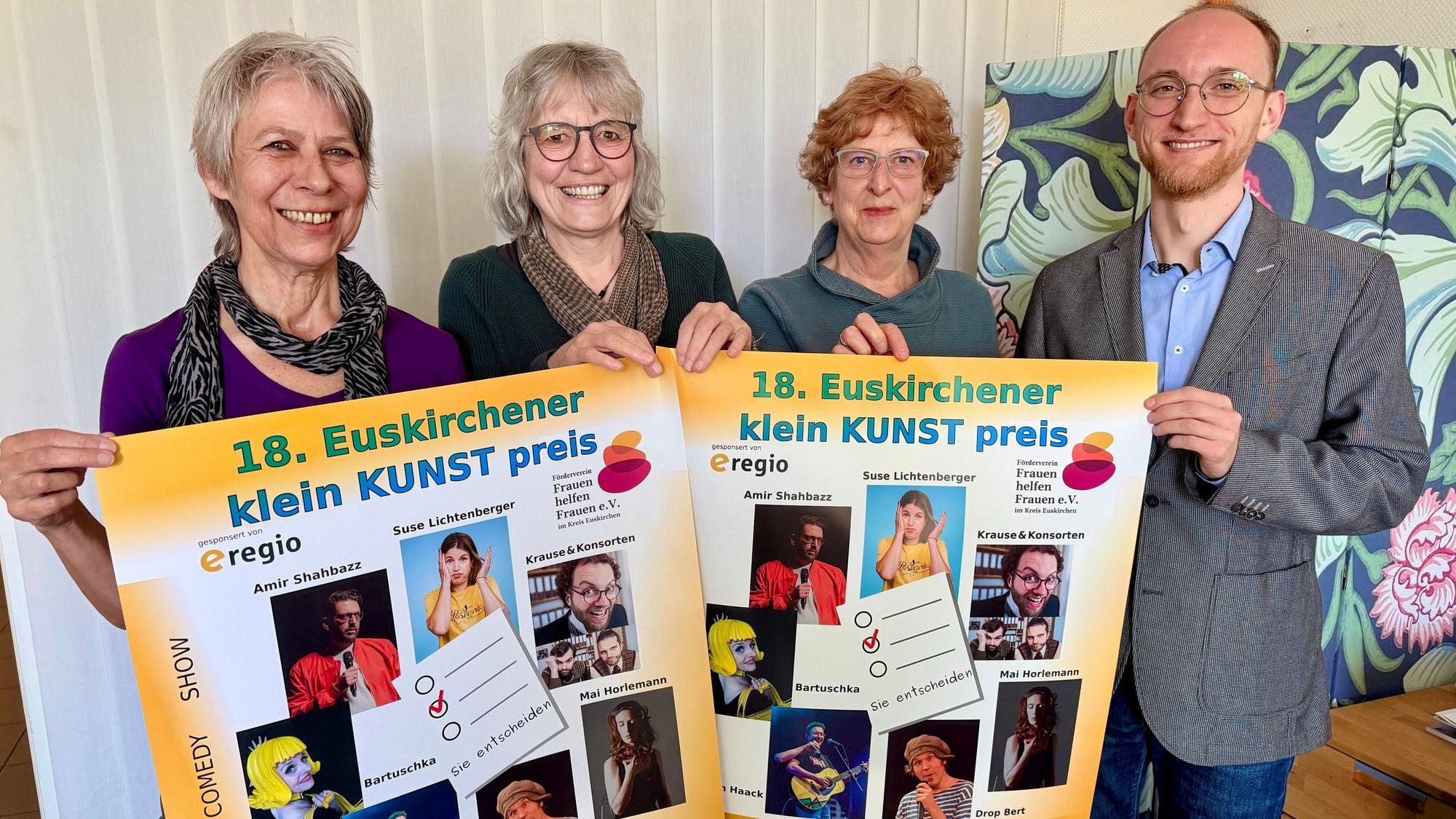 Drei Frauen aus dem Orga-Team und der Vertreter des Hauptsponsors e-regio stehen hinter Plakaten des Kleinkunstpreises und lachen in die Kamera.