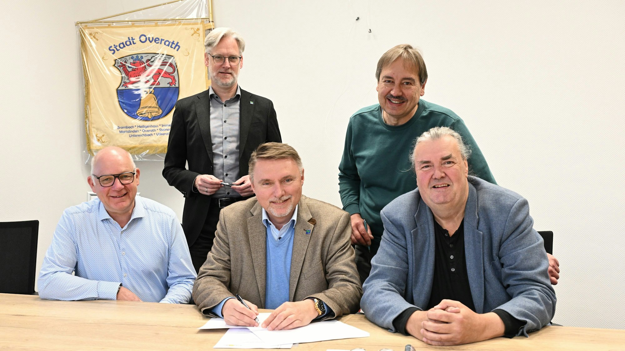 Eine Gruppe Männer sitzt vor einem Vertrag. Sie lächeln und unterzeichnen den Vertrag.