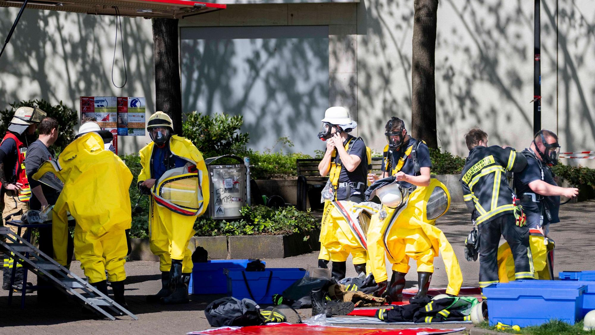 Das Bild zeigt zahlreiche Feuerwehrleute, die im Einsatz sind. Fünf von ihnen ziehen spezielle Schutzanzüge an.