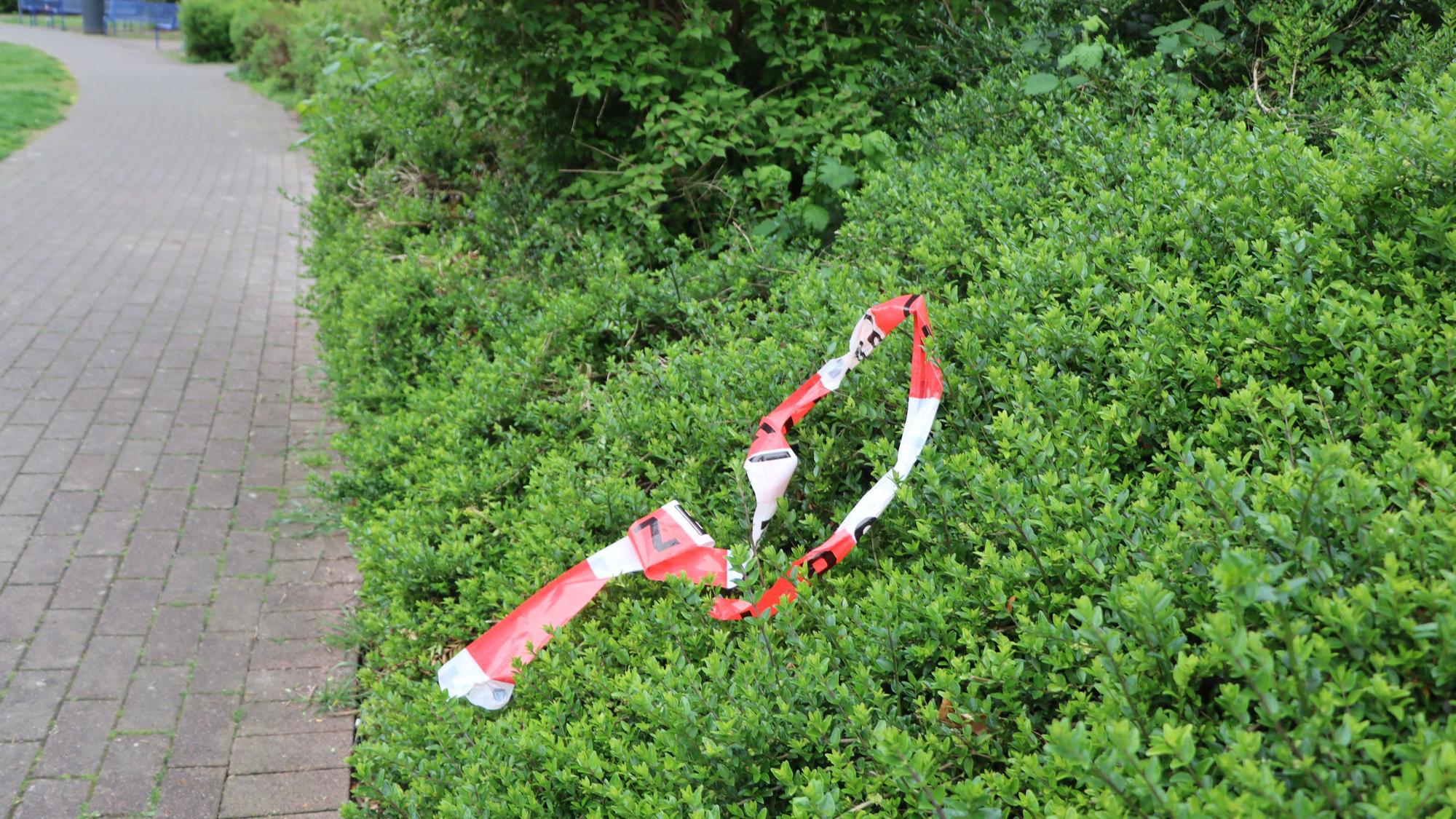 Ein Stück Absperrband liegt in einer Hecke.