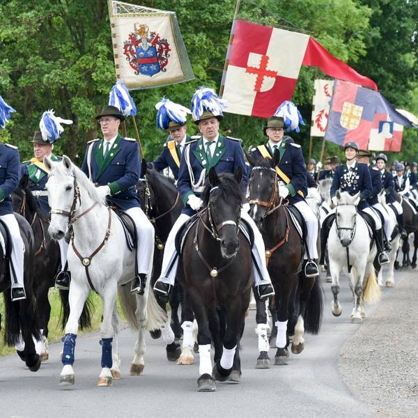 Zahlreiche Männer zu Pferd reiten über einen Feldweg.