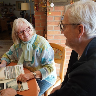 Das Foto zeigt eine ältere Frau und einen Mann, die sich Fotos auf einem Tisch anschauen.