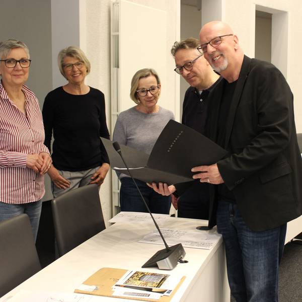 Männer und Frauen stehen an einem Tisch und halten schwarze Mappen.