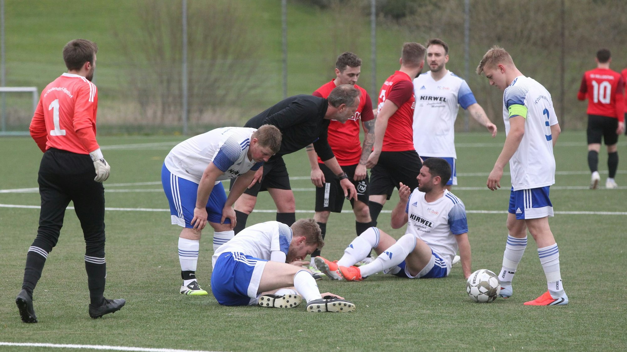 Das Bild zeigt zwei Fußballer, die nach einem Zweikampf auf dem Boden sitzen und sich verletzt haben.