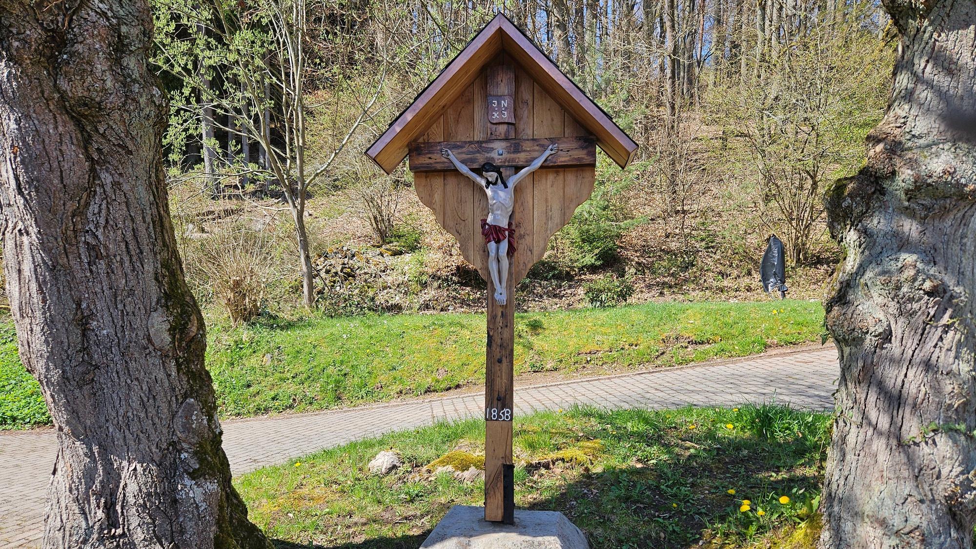 Das Foto zeigt das Wegekreuz, das von zwei Bäumen umrahmt wird.