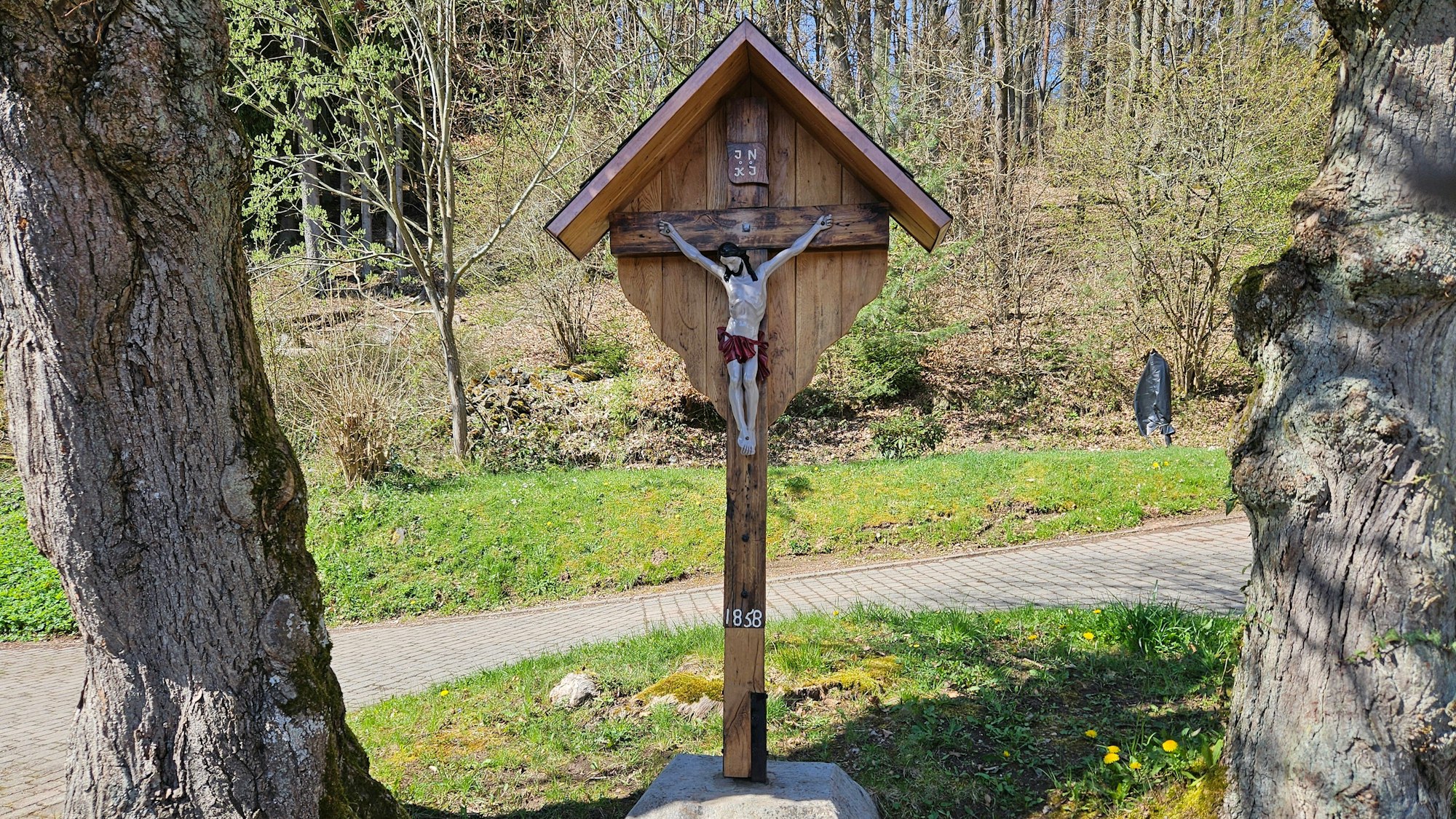 Das Foto zeigt das Wegekreuz, das von zwei Bäumen umrahmt wird.