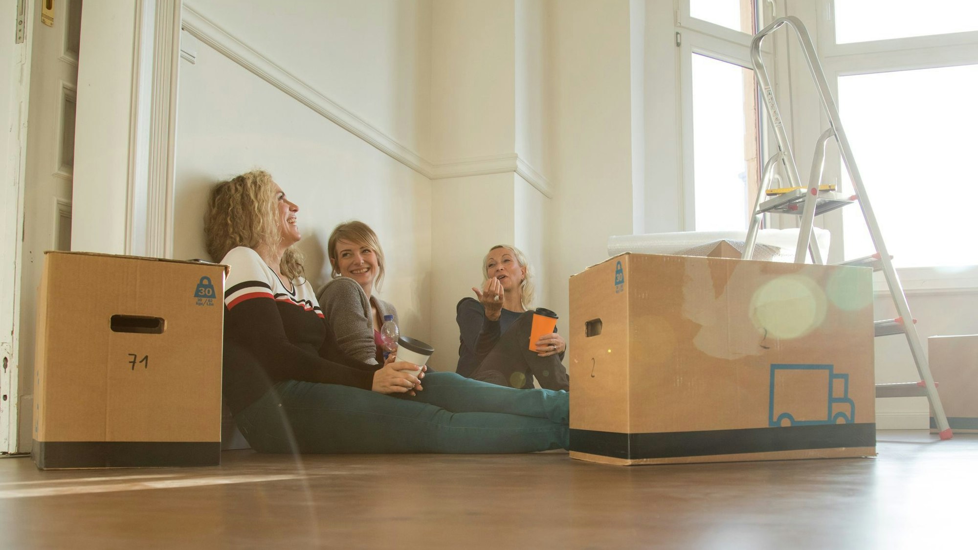 Drei Frauen sitzen gut gelaunt zwischen Umzugskisten