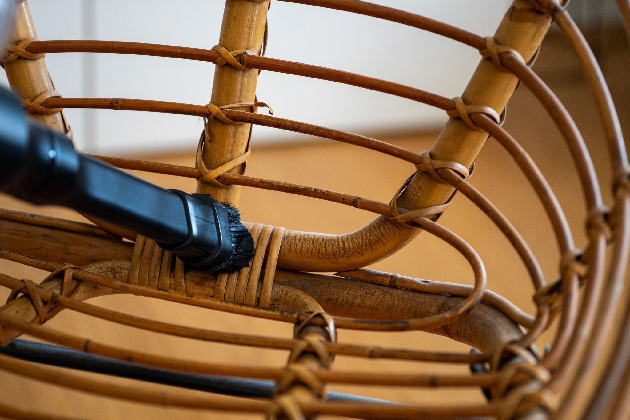 Ein Mann reinigt einen Rattansessel mit einem Staubsauger