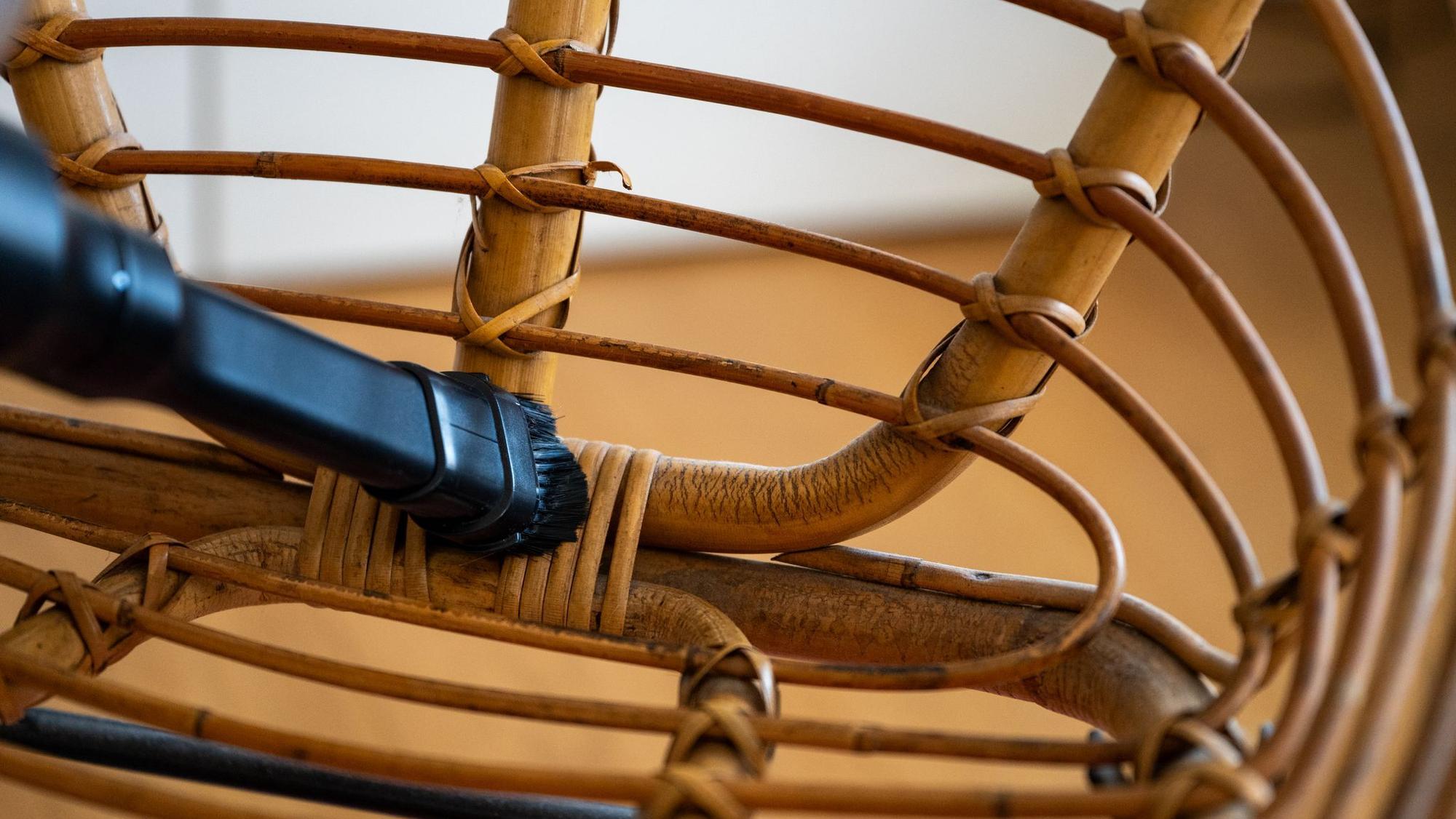 Ein Mann reinigt einen Rattansessel mit einem Staubsauger